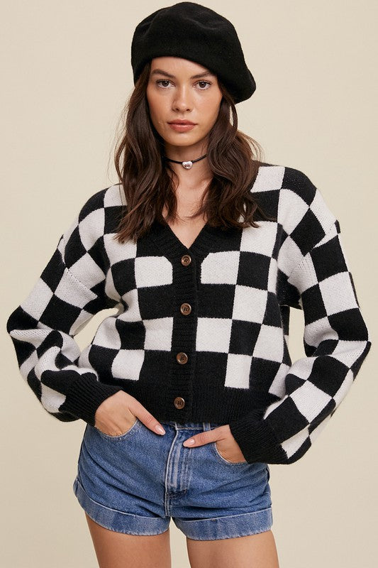 A cropped cardigan with a bold gingham pattern in [color(s)]. The cardigan has a V-neckline, long balloon sleeves with ribbed cuffs, and hidden side seam pockets. The model in the image is 5'8" with a 30-24-35 measurement and is wearing a size small.  The cardigan is made from a non-sheer, stretchy fabric blend and is machine washable.
