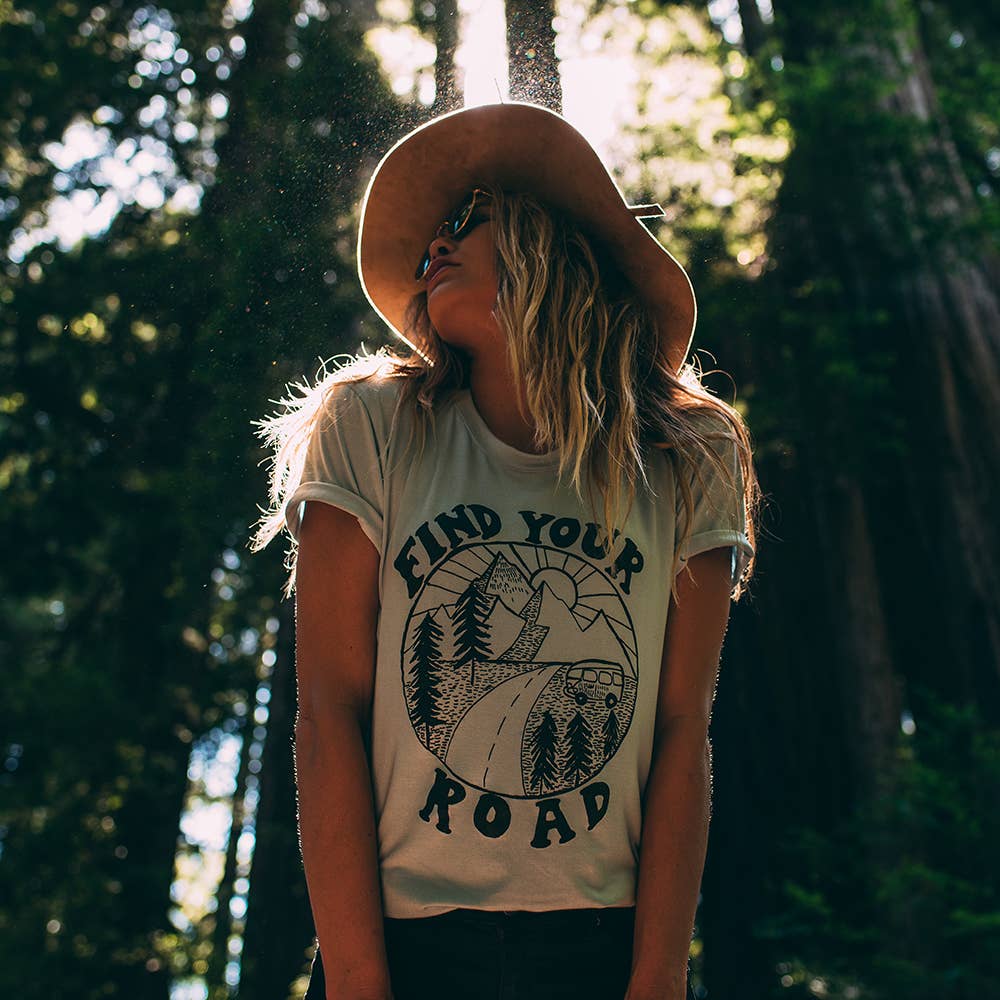 "Find Your Road" vintage-inspired graphic tee in dusty blue with a fitted crew neck. Model is wearing the tee tucked into jeans.